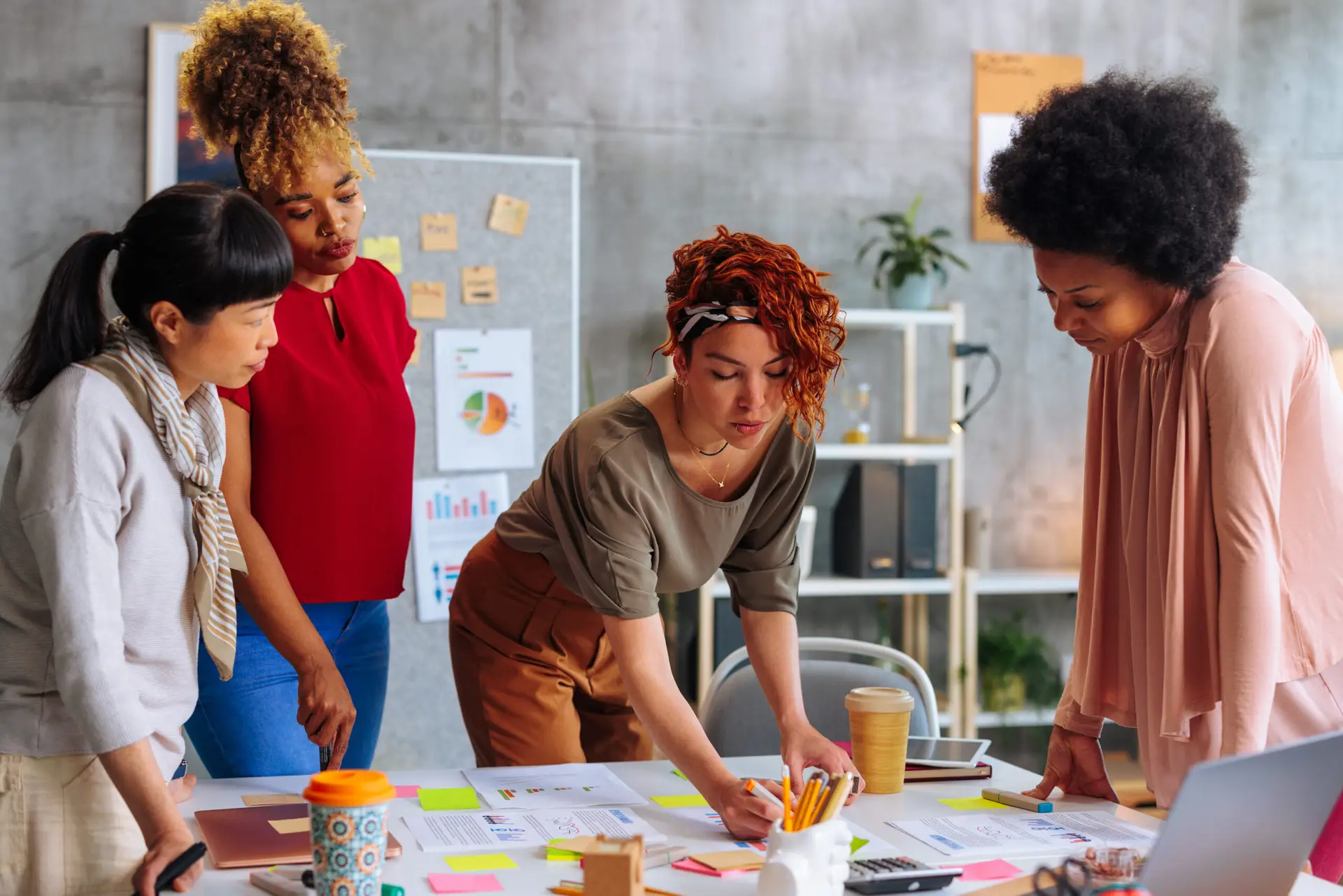 Four diverse young business women brainstorming together over the project development during a meeting in the boardroom.